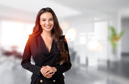 Photo for Smiling attractive businesswoman wearing formal wear standing holding hands together at office workplace in background. Concept of ambitious business person, inspired woman - Royalty Free Image