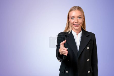 Téléchargez les photos : Smiling attractive businesswoman wearing formal wear standing stretching out hand for handshake near empty pale purple wall in background. Concept of ambitious business person, inspired woman - en image libre de droit
