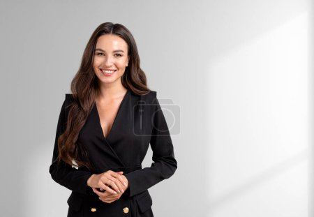 Photo for Smiling attractive businesswoman wearing formal wear standing holding hands together near empty white wall in background. Concept of ambitious business person, inspired woman - Royalty Free Image