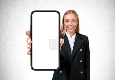 Photo for Smiling businesswoman showing phone with large mock up copy space screen, grey background. Concept of mobile app and social media - Royalty Free Image