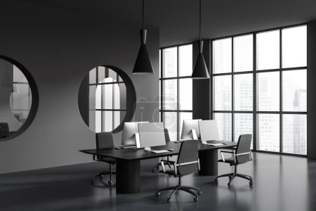 Foto de Dark coworking interior with pc desktop on table and armchairs, side view grey concrete floor. Business workplace with panoramic window. 3D rendering - Imagen libre de derechos