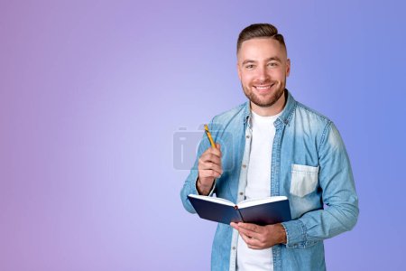 Téléchargez les photos : Dreaming handsome businessman wearing casual wear holding notebook and pen near empty purple wall in background. Concept of model, ambitious business person, student, learning - en image libre de droit