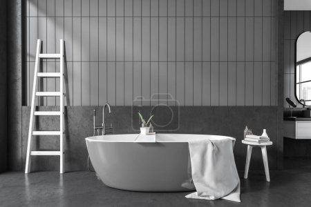 Téléchargez les photos : Front view on dark bathroom interior with bathtub, ladder, stool with shampoo and towels, grey walls, window in mirror reflection, concrete floor. 3d rendering - en image libre de droit