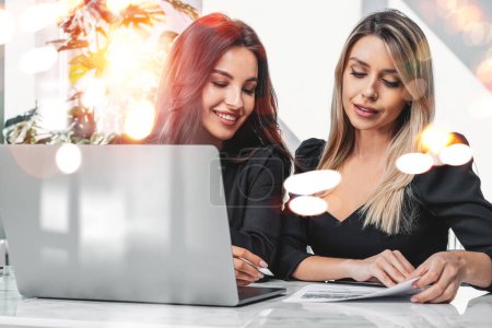 Foto de Two office women work together, laptop on desk in business room, analyzing financial report. Concept of business secretary and teamwork - Imagen libre de derechos