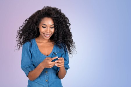 Téléchargez les photos : Happy black woman portrait typing in phone, empty copy space gradient background. Concept of online communication and mobile app - en image libre de droit