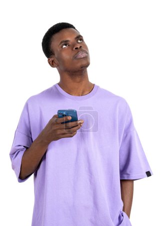 Téléchargez les photos : African man in purple t-shirt with phone in hand, thoughtful look up isolated over white background. Concept of dreams and plan - en image libre de droit