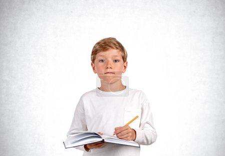 Photo for Pondering handsome boy in casual wear standing holding notebook and taking notes near empty white wall in background. Concept of inspired kid, education, learning, studying, student - Royalty Free Image