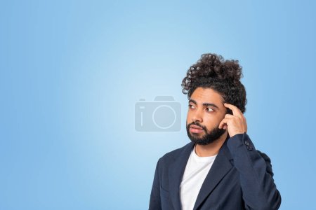 Téléchargez les photos : Dreaming handsome middle eastern arab businessman in formal wear touches his forehead with hand near empty blue wall. Concept of ambitious business person, student, learning, knowledge, thinking - en image libre de droit