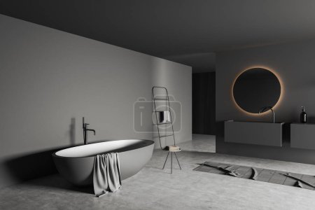 Téléchargez les photos : Vue d'angle sur l'intérieur sombre de la salle de bain avec miroir rond, baignoire, tabouret avec serviettes, tapis, murs gris, savon liquide. Rendu 3d - en image libre de droit