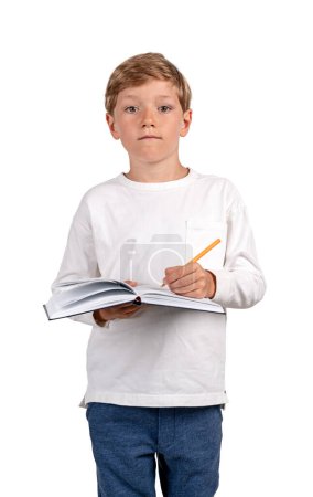 Téléchargez les photos : Enfant garçon avec stylo à la main, prenant des notes dans un carnet. Portrait d'enfant regardant la caméra, isolé sur fond blanc. Concept d'éducation et d'études - en image libre de droit
