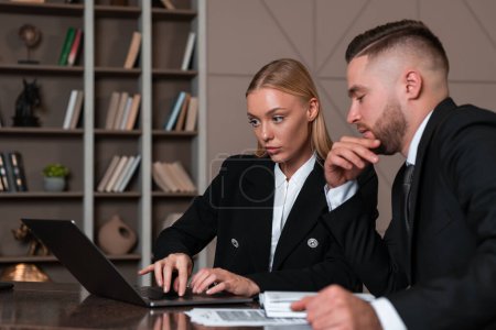 Foto de Businesswoman and businessman wearing formal wear sitting working on laptop taking notes at office workplace in background. Concept of teamwork, work together, business people, coworking, cooperation - Imagen libre de derechos