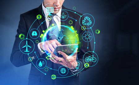 Foto de Businessman working with tablet, earth sphere glowing hologram and green energy icons circuit hud. Concept of resources and technology. - Imagen libre de derechos