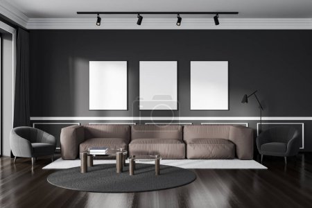 Foto de Interior oscuro salón relax con sofá y sillón, mesa de centro en la alfombra, suelo de madera. Espacio frío y tres carteles de maqueta en fila en la pared oscura. Renderizado 3D - Imagen libre de derechos