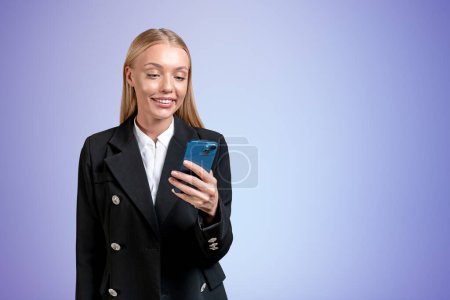 Foto de Sonriente atractiva mujer de negocios en ropa formal de pie sosteniendo teléfono inteligente cerca de la pared púrpura vacía en el fondo. Concepto de persona de negocios inspirada, mujer de ensueño, redes sociales, aplicación móvil - Imagen libre de derechos