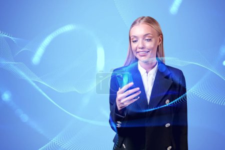 Téléchargez les photos : Smiling attractive businesswoman in formal wear standing holding smartphone near digital interface in background. Concept of inspired business person, dreaming woman, social media, mobile application - en image libre de droit