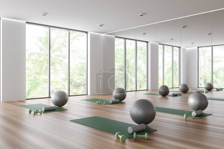 Téléchargez les photos : White yoga gym interior with mat and fitball with dumbbells, side view on hardwood floor. Fitness room corner with large mirror and panoramic window on tropics. 3D rendering - en image libre de droit