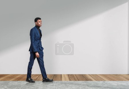 Téléchargez les photos : Homme d'affaires africain en costume bleu, regard cher, marchant sur le sol carrelage. Concept de développement de carrière et d'entreprise internationale. Espace de copie - en image libre de droit