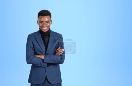 Téléchargez les photos : African American businesswoman smiling in suit, looking at the camera, arms crossed on light blue background. Concept of business offer. Copy space - en image libre de droit