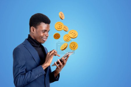 Téléchargez les photos : Homme d'affaires afro-américain tenant smartphone avec jeton crypto-monnaie. Fond bleu. Concept de banque en ligne, protection des données financières et de l'information, système innovant d'accumulation d'argent - en image libre de droit