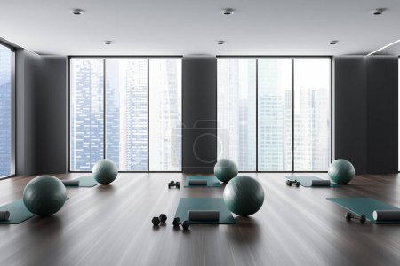 Téléchargez les photos : Dark modern sport class interior with yoga mat and fitball on hardwood floor. Fitness room with equipment and panoramic window on Singapore skyscrapers. 3D rendering - en image libre de droit