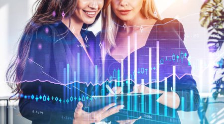 Foto de Dos mujeres de oficina con portapapeles en la sala de negocios, pantalla virtual con gráfico de barras del mercado de valores y candelabros de divisas. Concepto de análisis financiero - Imagen libre de derechos