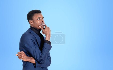 Photo for African businessman profile with thoughtful look, hand to chin. Manager making up plans and ideas, light blue background. Concept of problem and question. Copy space - Royalty Free Image