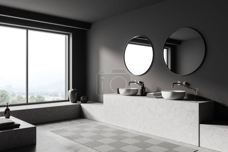 Téléchargez les photos : Intérieur salle de bain sombre avec double lavabo et miroir rond, vue latérale, tapis sur sol en béton gris. Fenêtre panoramique sur campagne, accessoires hôteliers sur pont. rendu 3D - en image libre de droit