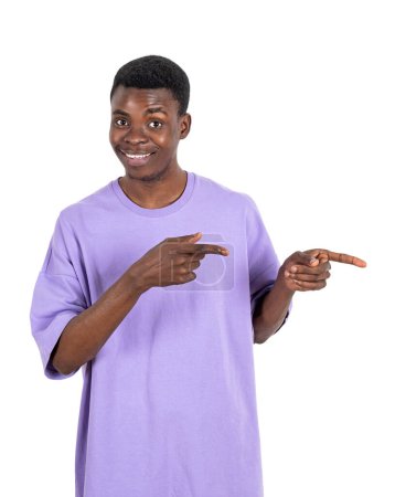 Foto de Retrato de hombre afroamericano en camiseta sonriente, dedo apuntando hacia un lado, aislado sobre fondo blanco. Concepto de oferta de redes sociales y negocios - Imagen libre de derechos