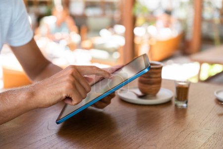 Téléchargez les photos : Businessman doigt tactile écran de tablette, bureau en bois avec boisson, fond flou de café d'été à l'extérieur. Concept d'entreprise en ligne et de médias sociaux - en image libre de droit