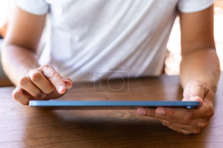 Foto de Hombre en camiseta blanca, primer plano dedo toque tableta en mesa de madera. Concepto de negocio en línea, redes sociales, compras, aplicación móvil - Imagen libre de derechos