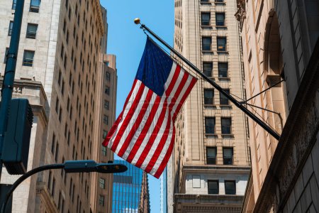 Téléchargez les photos : Drapeau américain contre bâtiment dans le centre-ville de New York, Manhattan. Wall Street et drapeau américain parmi les différents bâtiments - en image libre de droit