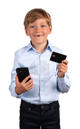 Téléchargez les photos : Écolier souriant avec téléphone et carte de crédit dans les mains, portrait isolé sur fond blanc. Concept d'application mobile et de paiement en ligne - en image libre de droit