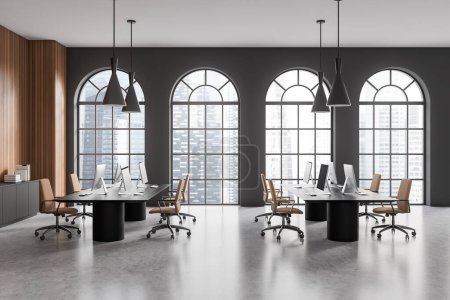 Photo for Interior of modern open space office with gray and wooden walls, concrete floor, long black computer tables, gray file cabinet and arched windows with blurry cityscape. 3d rendering - Royalty Free Image