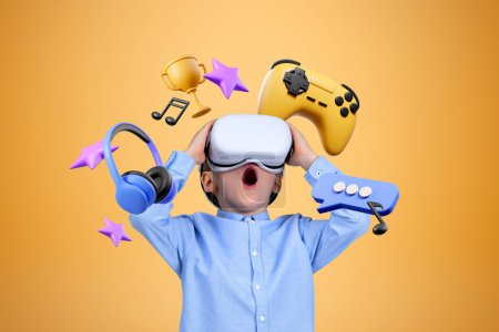Téléchargez les photos : Étonné petit garçon en VR lunettes debout sur orange bleu avec des jeux vidéo et des icônes multimédia au-dessus de lui. Concept d'internet pour la joie - en image libre de droit