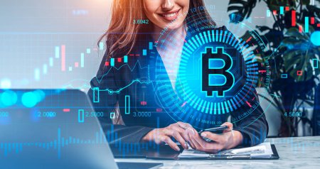 Photo for Businesswoman smiling, smartphone and laptop on desk. Cryptocurrency hologram with bitcoin and binary, bar chart and lines. Concept of internet banking - Royalty Free Image