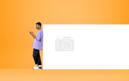 Photo for Black man working with phone, texting on yellow background. Concept of online communication and mobile app. Mock up copy space whiteboard - Royalty Free Image