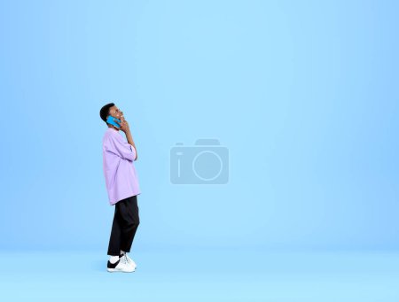 Photo for African American handsome businessman wearing casual wear is talking on smartphone near empty blue wall in background. Concept of working process, distance work, important conference call - Royalty Free Image