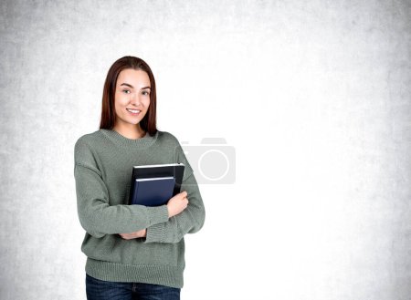 Photo for Attractive businesswoman wearing casual wear is standing holding notebook near empty white wall in background. Concept of working process, taking notes for daily schedule, scorekeeper and secretary - Royalty Free Image