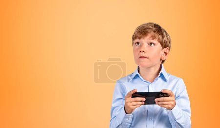 Photo for Portrait of serious little boy in formal clothes holding smartphone over orange background. Concept of social media and e learning. Mock up - Royalty Free Image