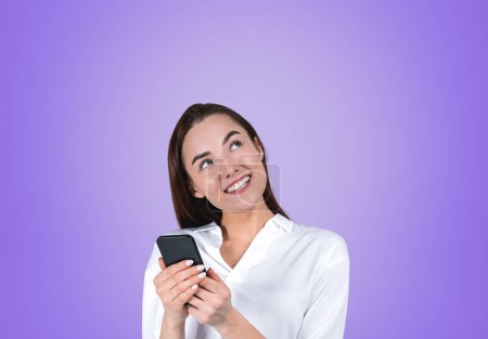 Foto de Mujer de negocios sonriente trabajando con el teléfono, pensando y soñando retrato sobre fondo púrpura. Concepto de conexión y redes sociales. Copiar espacio - Imagen libre de derechos