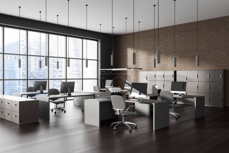 Foto de Esquina de la moderna oficina de espacio abierto con paredes de ladrillo gris y marrón, suelo de madera oscura, fila de mesas de ordenador con sillas grises y gabinetes beige. renderizado 3d - Imagen libre de derechos