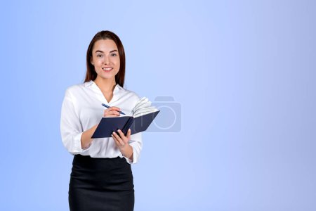 Photo for Smiling businesswoman take note in notebook in hands, light blue background. Concept of schedule and time management. Copy space - Royalty Free Image