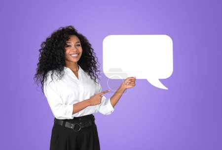 Photo for African American businesswoman wearing formal wear is standing pointing up with fingers to speech bubble icon near empty purple wall in background. Concept of model, successful business person, show - Royalty Free Image