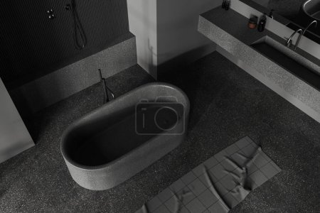 Téléchargez les photos : Vue de dessus de l'intérieur de la salle de bain sombre avec baignoire, lavabo et douche. Espace ouvert coin de bain avec accessoires et serviette de pieds sur sol en béton gris. rendu 3D - en image libre de droit