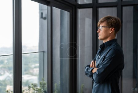 Téléchargez les photos : Portrait d'un jeune homme d'affaires européen confiant, les bras croisés, regardant par la fenêtre du bureau. Concept de leadership - en image libre de droit