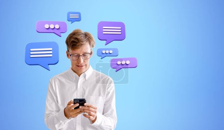 Foto de Feliz hombre de negocios usando teléfono, mensajes de texto burbujas de voz sobre fondo azul. Concepto de redes sociales, comunicación empresarial y mensajero - Imagen libre de derechos