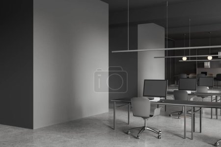 Foto de Esquina de la moderna oficina de espacio abierto con paredes grises, piso de hormigón, fila de mesas de ordenador con sillas grises y se burlan de la pared a la izquierda. renderizado 3d - Imagen libre de derechos