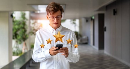 Photo for Serious young European businessman with smartphone giving fiver star rank in blurry hotel lobby. Concept of giving service feedback and rating - Royalty Free Image