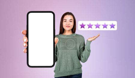 Photo for Smiling young woman hand showing a mockup phone screen, purple background. Giving five stars, high rating and share her positive experience. Concept of review and customer service - Royalty Free Image