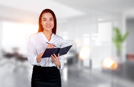 Photo for Smiling businesswoman take note in notebook in hands, office room on blurred background. Concept of plan and business idea - Royalty Free Image